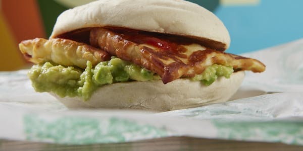 LEON Smashed Avocado and Halloumi Muffin on LEON paper, with colourful LEON logo in the background